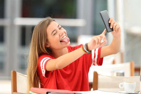Single happy student taking selfie with a smart phone sitting in a coffee shop terraceの写真素材