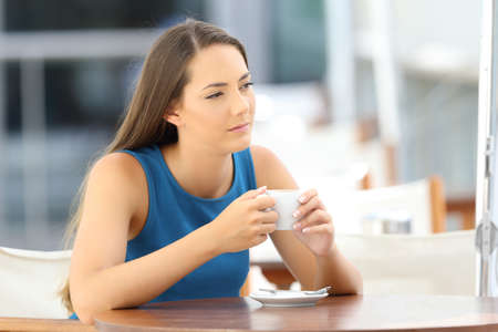 Single pensive woman alone holding a coffee mug sitting in a barの写真素材