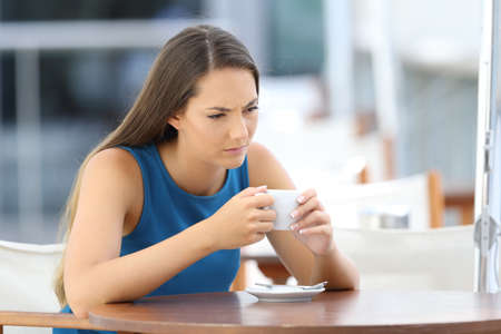 Single angry woman thinking and holding a cup sitting in a bar terraceの写真素材