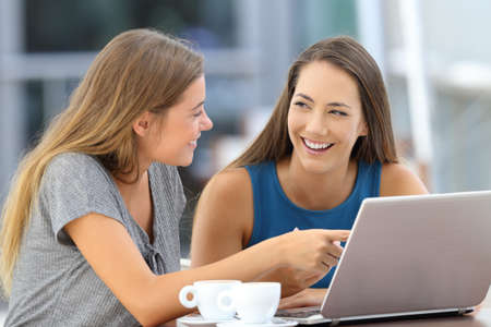 Two happy friends talking about on line content sitting in a bar terraceの写真素材