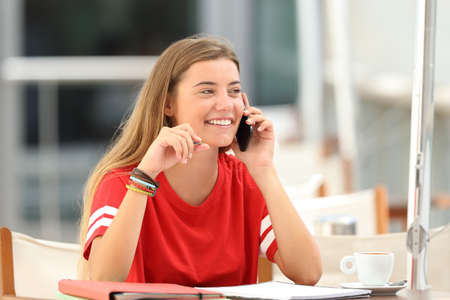 Candid student girl laughing talking on phone siting in a bar terraceの写真素材