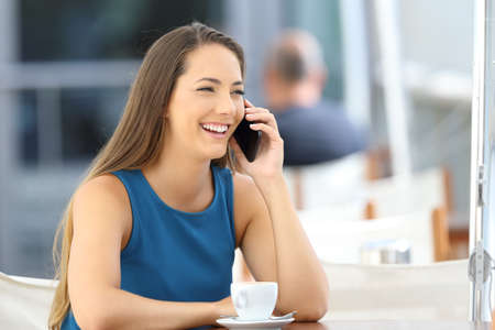 Single woman having a phone conversation sitting in a bar terraceの写真素材