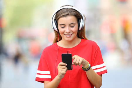 Front view of a single teen girl walking and listening music on the streetの写真素材
