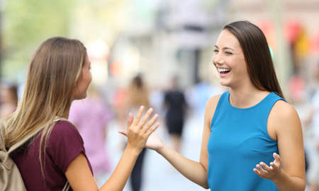 Two happy friends greeting and meeting on the streetの写真素材