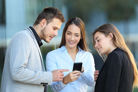 Group of three executives talking and checking a mobile phone on the streetの写真素材