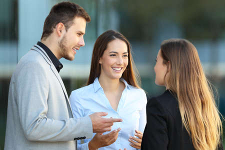 Three happy executives standing talking on the street with an office building in the backgroundの写真素材