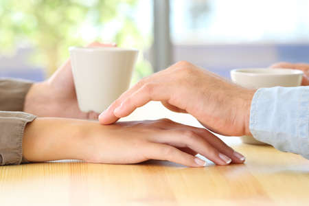 Close up of a man touching the hand of his partner during a date in a table of a coffee shop or homeの写真素材