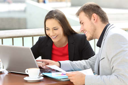 Two executives working on line with a laptop sitting in a bar terraceの写真素材