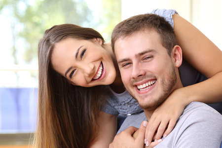 Happy couple smiling together with perfect teeth and looking at camera at homeの写真素材