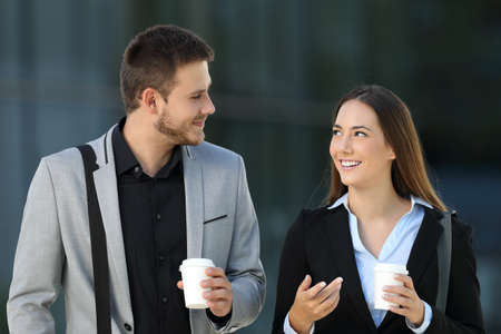 Front view of a happy couple of executives walking and talking on the street with an office building in the background