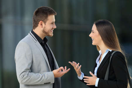 Side view portrait of a happy couple of executives talking on the street