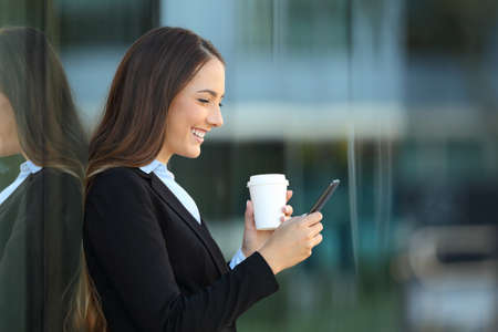 Profile of an executive using a smart phone on the street with an office building in the backgroundの写真素材