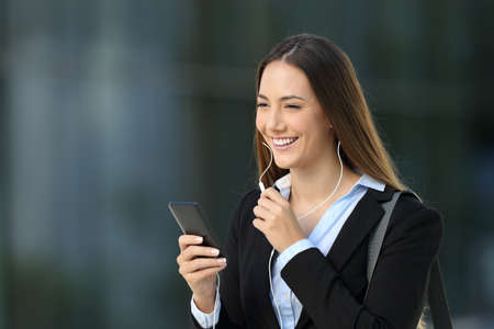 Happy executive talking with earphones during a phone call on the street with an office building in the backgroundの写真素材