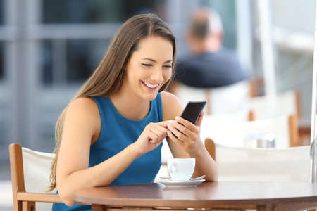 Happy woman using a smart phone alone sitting in a bar terraceの写真素材