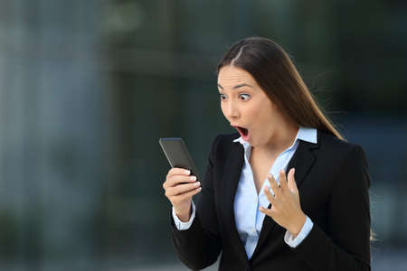 Single excited executive reading amazing news on line in a smart phone on the streetの写真素材