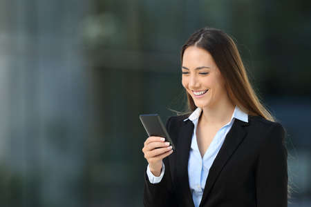 Single smiley executive woman using a mobile phone walking on the streetの写真素材