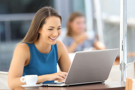 Happy woman writing in a laptop alone sitting in a bar terraceの写真素材