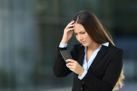 Worried executive reading bad news in a cellphone on the street with an office building in the backgroundの写真素材