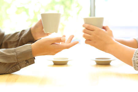 Side view close up of two women hands talking in a bar or house holding coffee cupsの写真素材