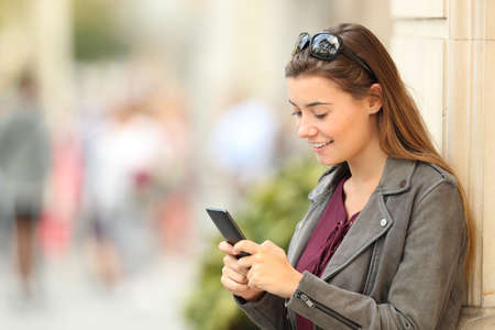 Single fashion girl texting in a smart phone leaning on a building wall outdoors on the streetの写真素材