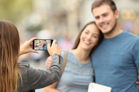 Three happy friends taking photos with a smart phone outside on the streetの写真素材