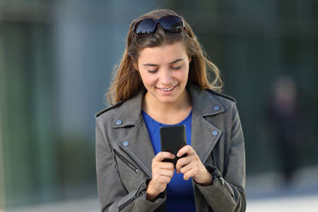 Front view portrait of a happy girl using a smart phone walking outdoors on the streetの写真素材