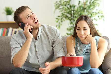 Upset couple sitting in a couch in the living room and calling insurance for home leaksの写真素材