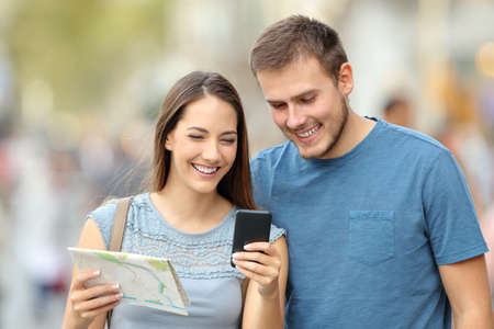 Front view of a couple of happy tourists searching location on line with a phone and map on the streetの写真素材