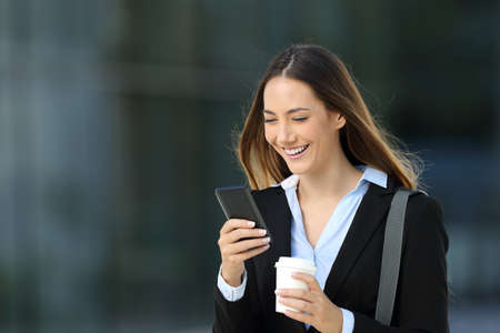 Single executive checking content in a smart phone and holding a take away coffee walking on the streetの写真素材