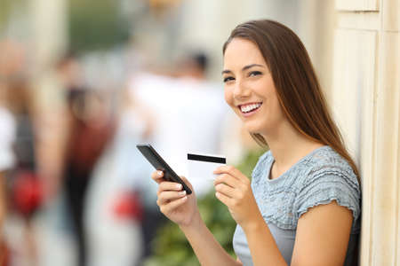 Portrait of an on line shopper looking at camera and holding a credit card on the streetの写真素材