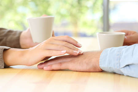 Close up of a couple dating and touching hands in a bar or houseの写真素材