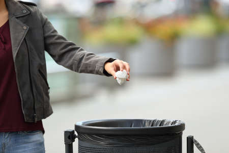 Close up of a lady hand throwing garbage to a trash bin on the streetの写真素材