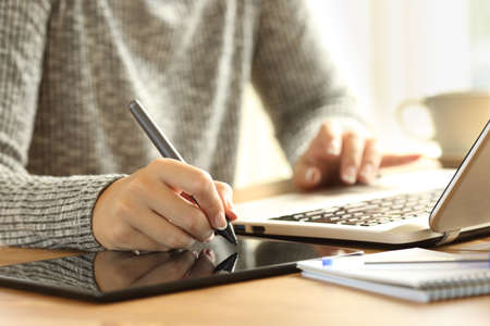 Close up of a designer woman working drawing with a digital pen on a tablet and a a laptop on a deskの写真素材