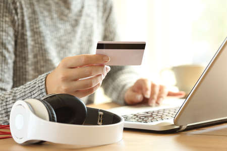 Close up of an on line buyer hands buying music with a laptop and credit card at home