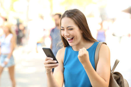 Excited woman reading amazing news on line in a smart phone on the streetの写真素材
