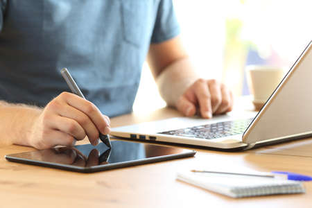 Close up of a man hand drawing with a display pen and a laptop on a desk at home or officeの写真素材