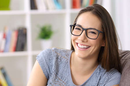 Portrait of a happy woman wearing eyeglasses smiling at camera sitting on a sofa at homeの写真素材