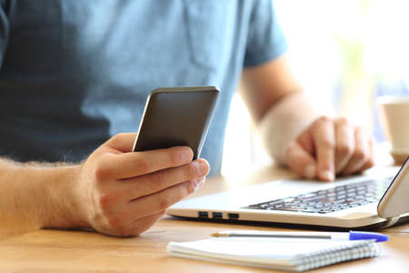 Close up of a man hands using a smart phone and a laptop on a desktop at home or office