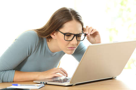Woman suffering eyesight problems trying to read on line content from a laptop at homeの写真素材