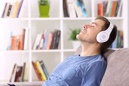 Side view portrait of a man relaxing sitting on a couch at home listening to music wearing headphonesの写真素材
