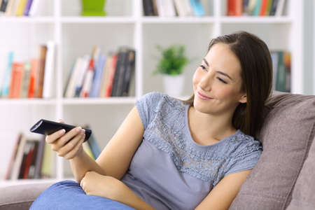 Woman watching tv holding remote control sitting on a sofa at home