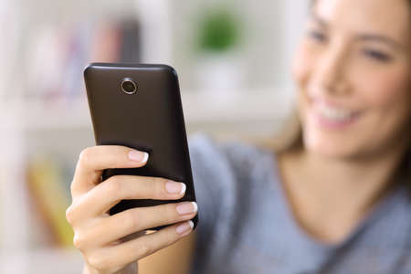 Close up of a woman hand using a smart phone with a blurred face and background at homeの写真素材