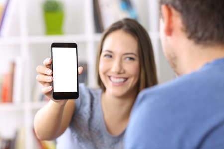 Woman showing a smart phone screen to a friend at homeの写真素材