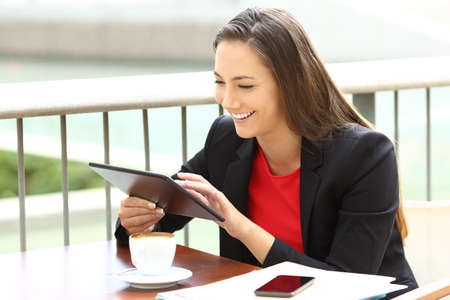 Single executive working on line using a tablet sitting in a bar terraceの写真素材