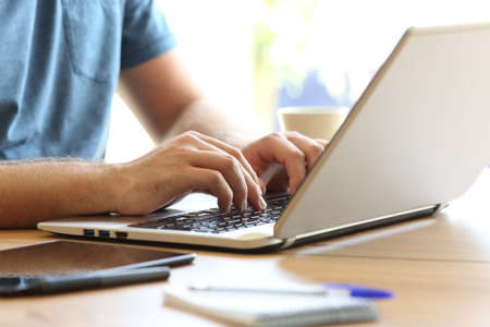 Close up of man hands typing on a laptop keyboard on a desk at home or officeの写真素材