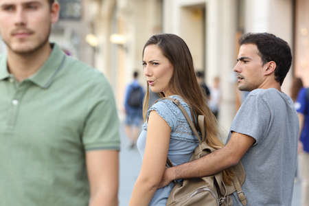 Disloyal woman looking another man and her angry boyfriend looking at her on the streetの写真素材
