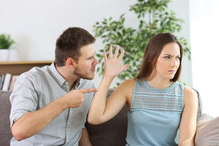 Angry couple fighting sitting on a couch at homeの写真素材