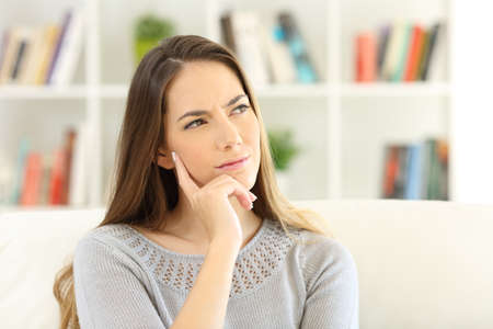 Front view portrait of a woman wondering sitting on a sofa at home