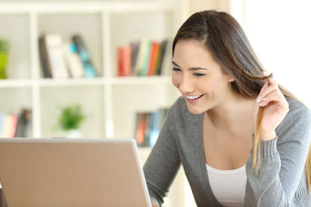 Candid girl dating on line with a laptop and touching hair sitting at homeの写真素材
