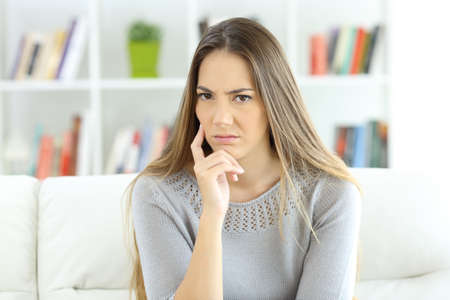 Front view portrait of a suspicious woman looking at camera sitting on a sofa at homeの写真素材